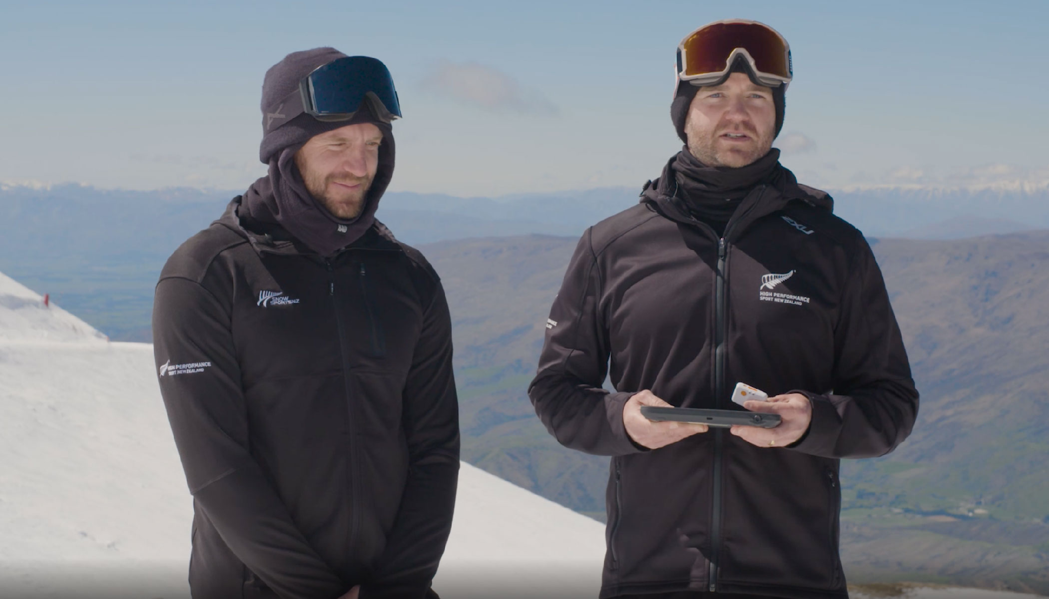 Sean and Cameron on a ski slope holding wearable tech